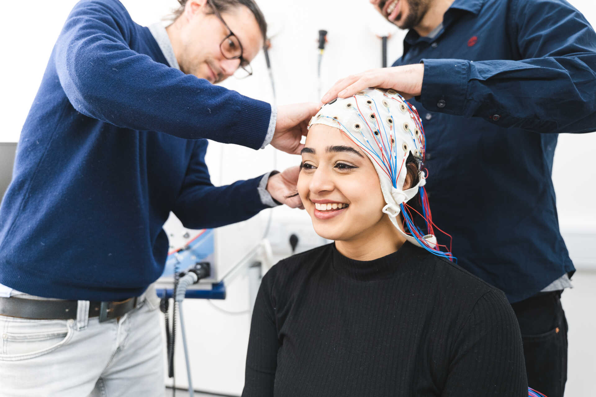 Researchers fit an electroencephalography cap with sensors and wires on a participant in a neuroscience laboratory.