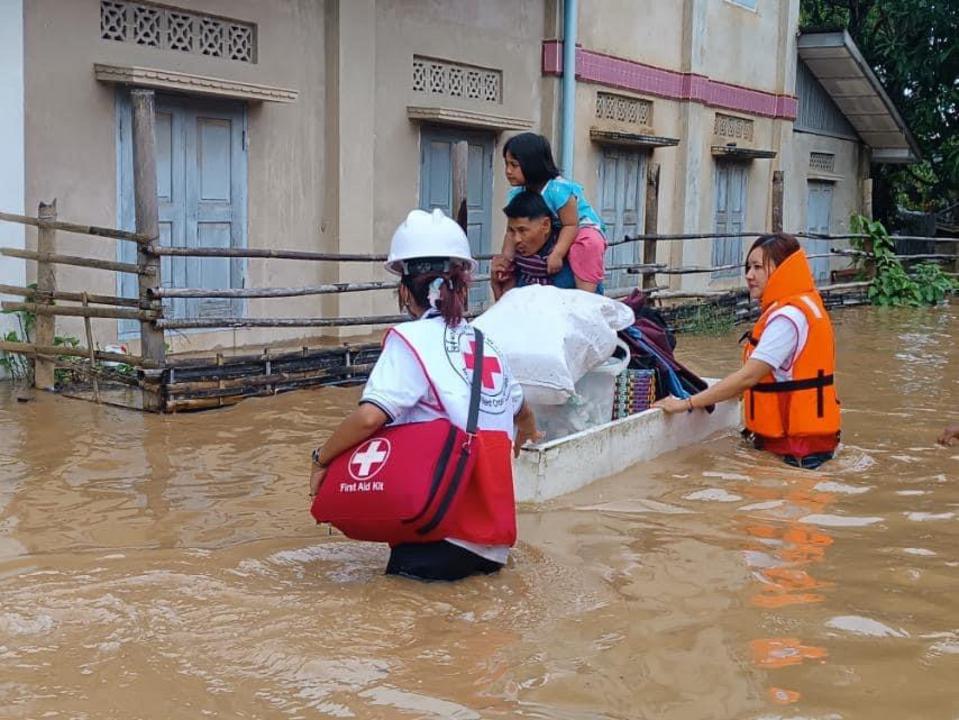 Voluntarios civiles de la Cruz Roja de Myanmar evacúan a una familia y sus pertenencias por un barrio inundado.