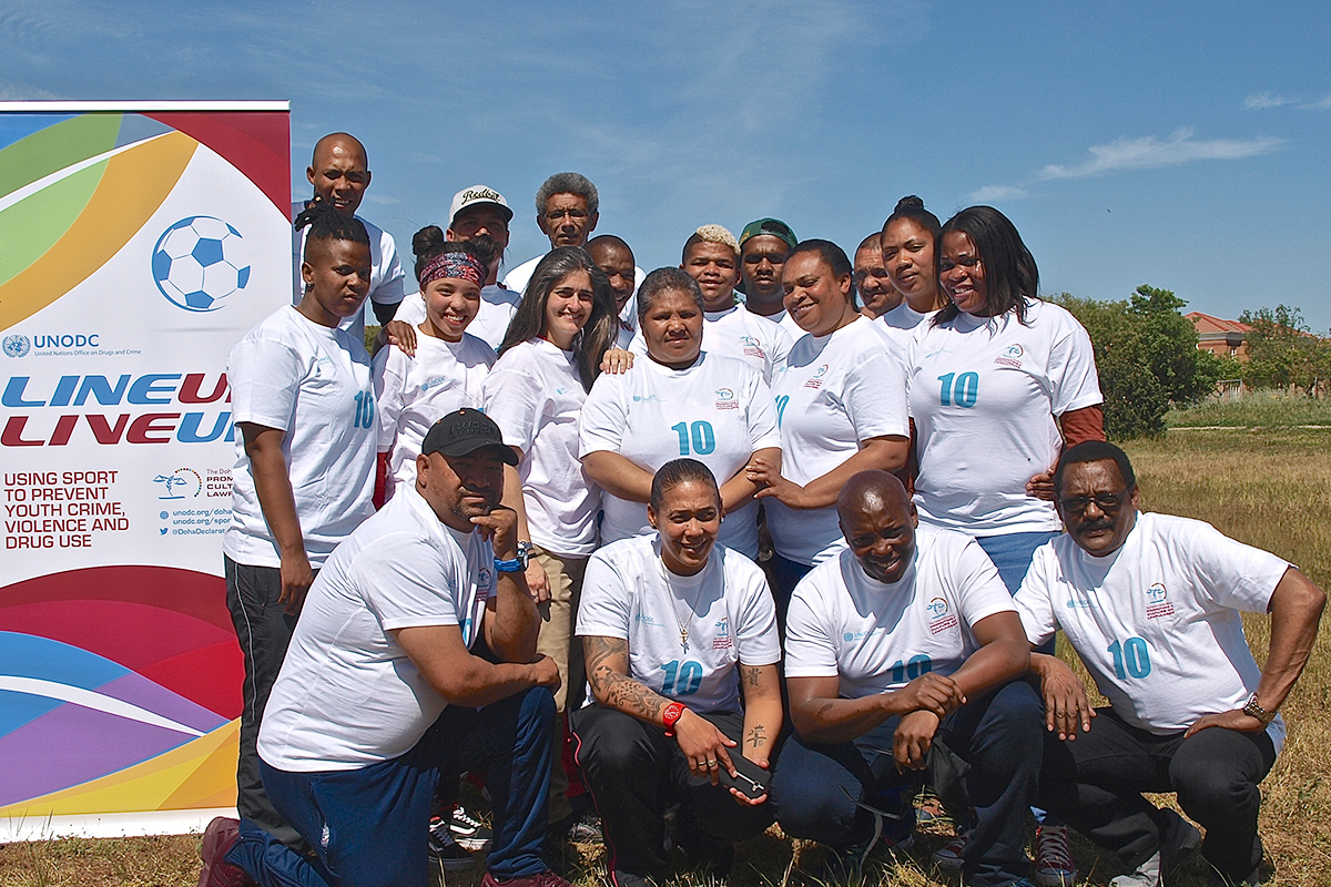 Participantes civiles de una formación de prevención del delito posan junto a un cartel de Line Up Live Up que promueve el deporte para prevenir la delincuencia juvenil, la violencia y el consumo de drogas.